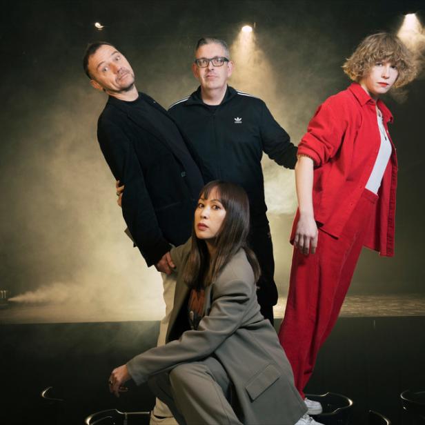 Die Band International Teachers of Pop posiert auf einer Bühne mit Nebel im Hintergrund.