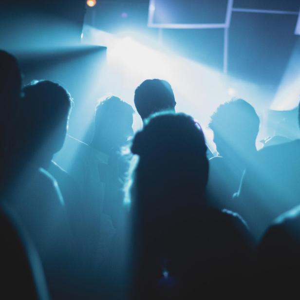 Silhouetten von Menschen stehen im blauen Licht eines Veranstaltungsortes.