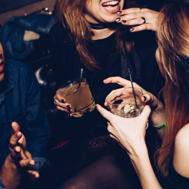 Drei junge Leute sitzen in einer Bar und halten Cocktails in den Händen.