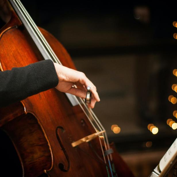 Ein Cellist spielt vor einem Notenständer mit Bokeh-Lichtern im Hintergrund.