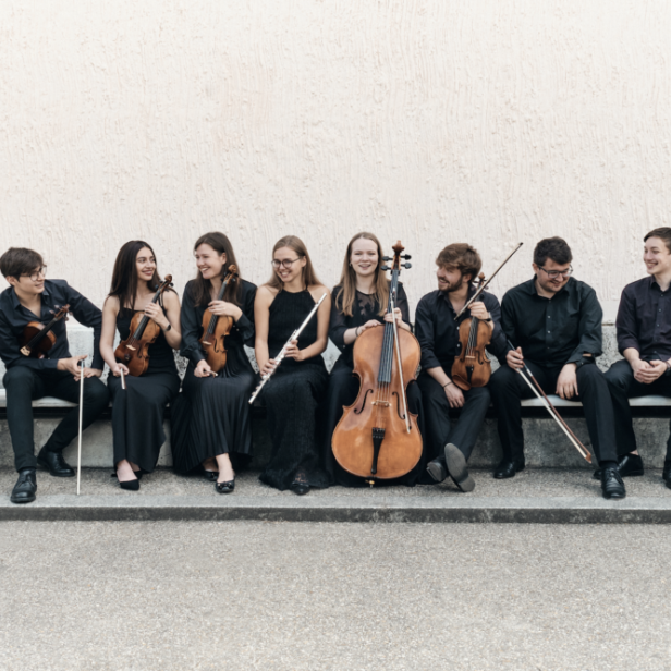 Ein Ensemble aus jungen Musikern sitzt mit ihren Instrumenten auf einer Bank.