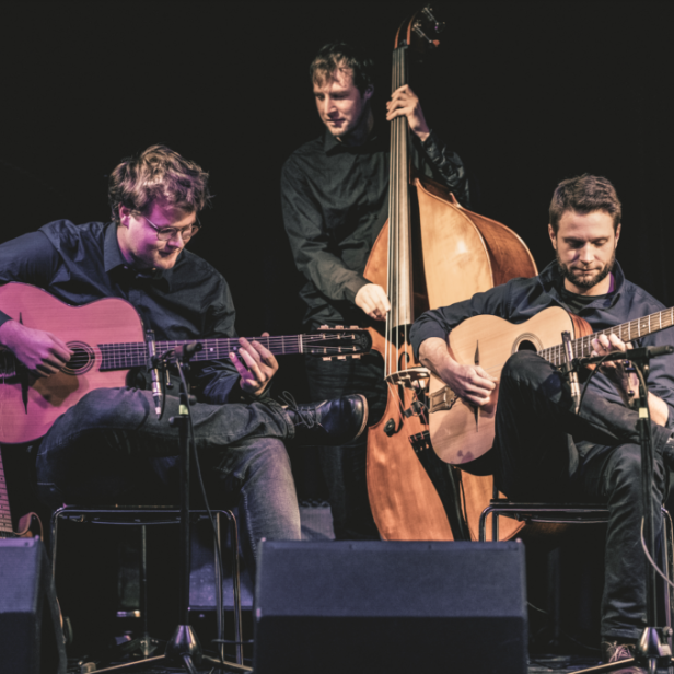 Drei Musiker spielen Gitarre und Kontrabass auf einer Bühne.