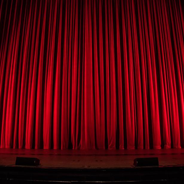 Ein roter Theatervorhang auf einer dunklen Bühne.