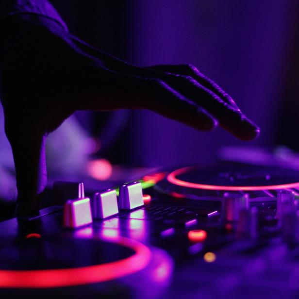 Eine Hand bedient ein DJ-Mischpult mit roter und violetter Beleuchtung.