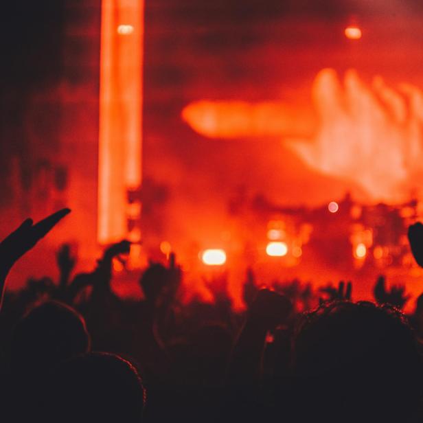 Eine Menschenmenge jubelt bei einem Konzert mit roter Bühnenbeleuchtung.