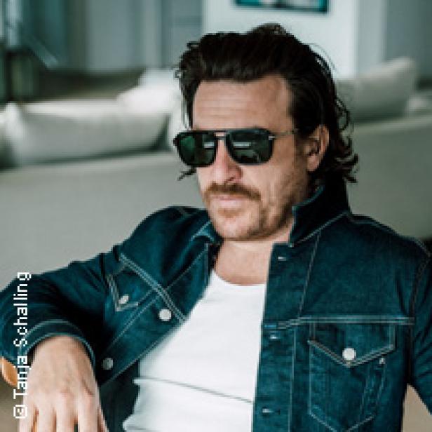 Ein Mann mit Sonnenbrille und Jeansjacke sitzt lässig da.