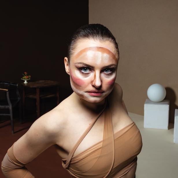 Eine Frau mit Make-up-Konturierung im Gesicht posiert selbstbewusst.