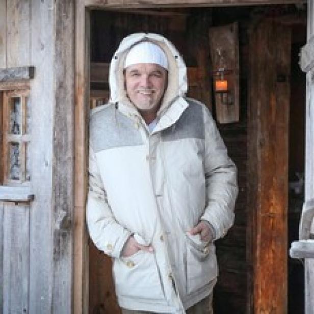 DJ Ötzi steht vor einer Holzhütte im Schnee.