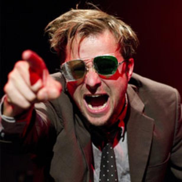 Ein Mann mit Sonnenbrille und Anzug gestikuliert und schreit.