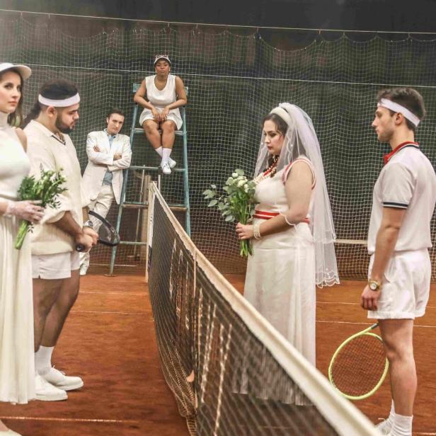 Eine Hochzeitsgesellschaft in Tenniskleidung steht auf einem Tennisplatz.