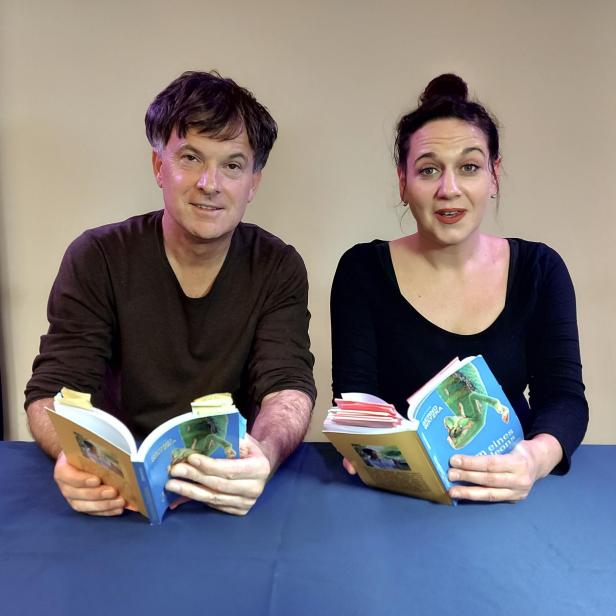 Ein Mann und eine Frau sitzen an einem Tisch und lesen ein Buch über Chamäleons.