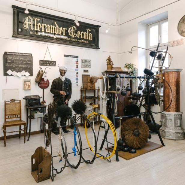 Ausstellungsraum mit Werkzeugen und Ausrüstung eines Schornsteinfegers, darunter ein Schaufensterpuppe in Arbeitskleidung.