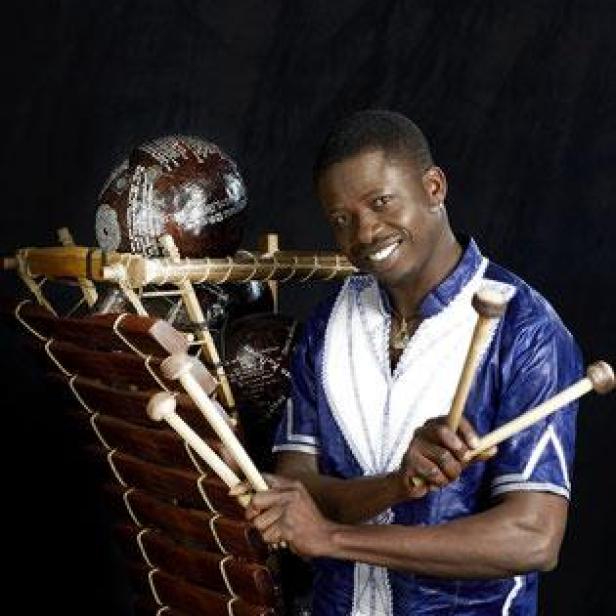 Ein Mann mit Schlägeln steht neben einem Balafon und lächelt.
