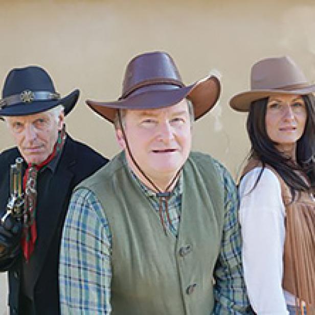 Drei Personen in Cowboy-Kostümen stehen nebeneinander.