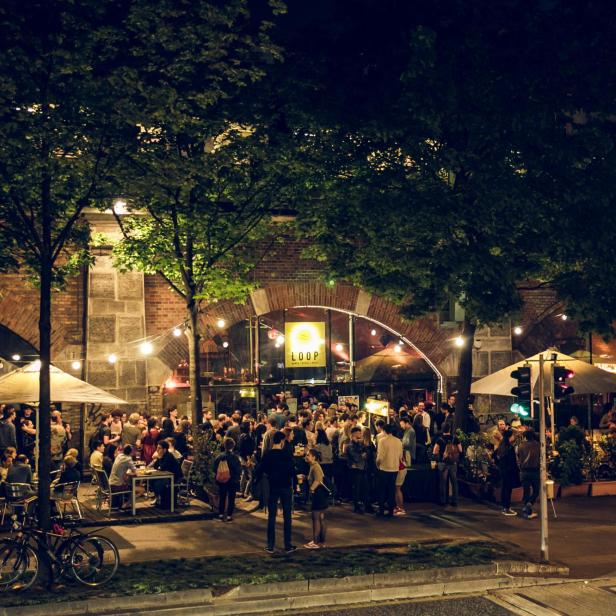 Am Abend sitzen und stehen viele Menschen vor dem Eingang des „Loop“.