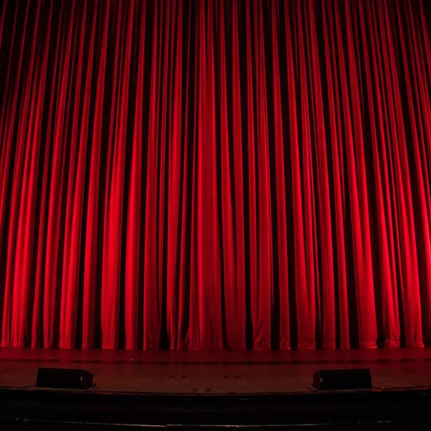 Ein roter Theatervorhang auf einer dunklen Bühne.