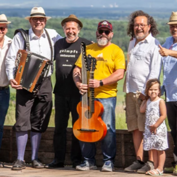 Eine Gruppe von Musikern mit Akkordeon und Gitarre posiert mit einem kleinen Mädchen vor einer Landschaft.