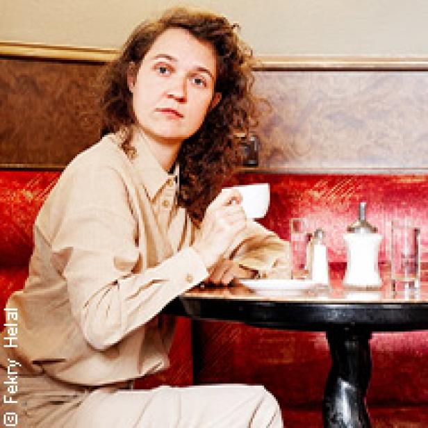 Eine Frau sitzt in einem Café und hält eine Tasse in der Hand.