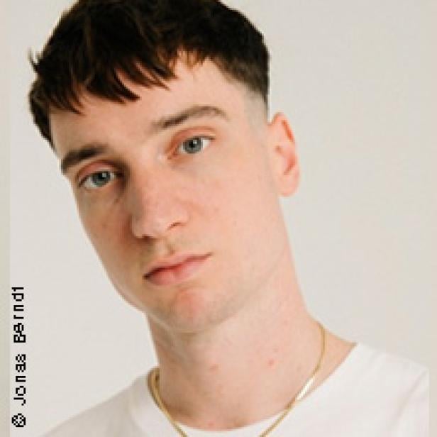 Ein Porträt eines jungen Mannes mit kurzen, dunklen Haaren und hellen Augen.