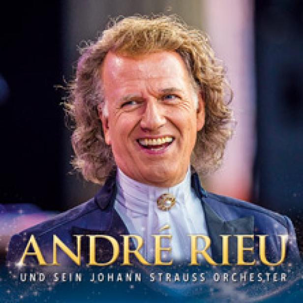 André Rieu lächelt in einem blauen Anzug vor einem verschwommenen Hintergrund.