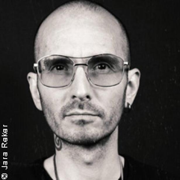 Ein Mann mit Brille und rasiertem Kopf blickt in die Kamera.