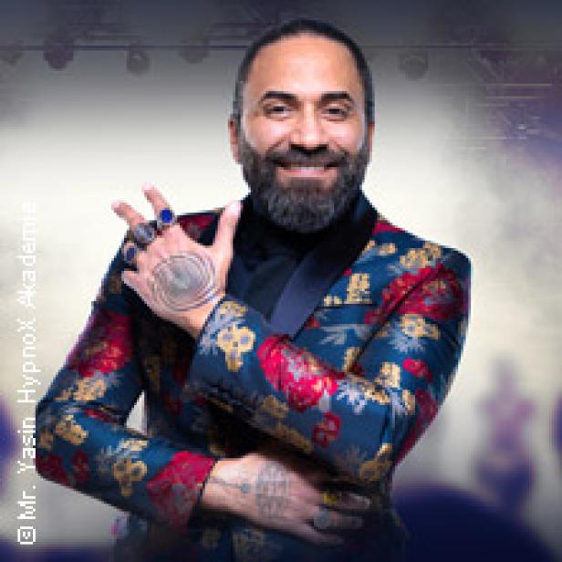 Ein Mann mit Bart und auffälligem Sakko lächelt in die Kamera.