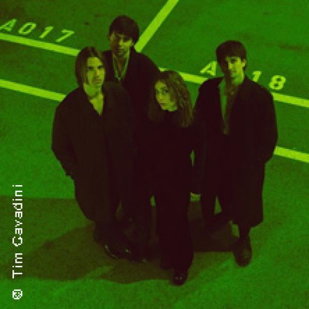 Eine Band steht in dunkler Kleidung auf einem Parkplatz.