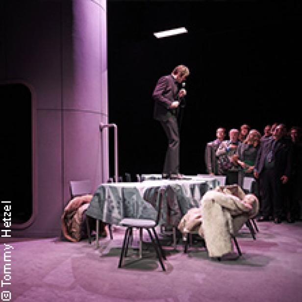 Ein Mann steht auf einem Tisch und spricht vor einer Gruppe von Menschen.