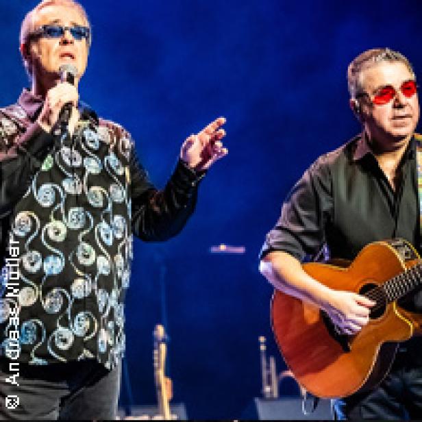 Zwei Männer stehen auf einer Bühne, einer singt ins Mikrofon, der andere spielt Gitarre.