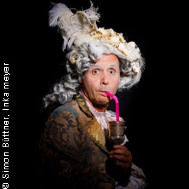 Ein Mann in historischer Kleidung und Perücke trinkt mit einem pinkfarbenen Strohhalm aus einem Kelch.