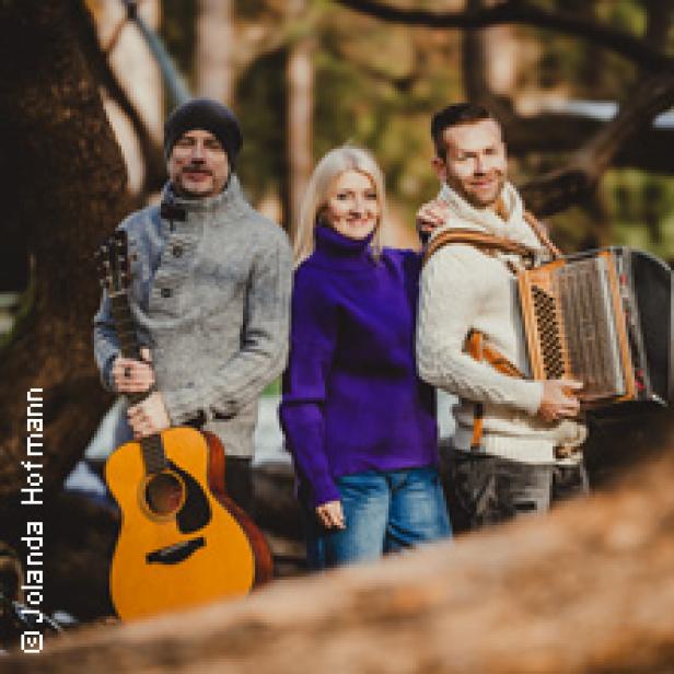 Eine Musikgruppe posiert mit Gitarre und Akkordeon im Wald.