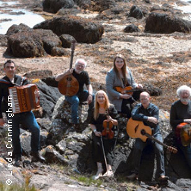 Eine Musikgruppe sitzt mit ihren Instrumenten auf Felsen am Ufer.