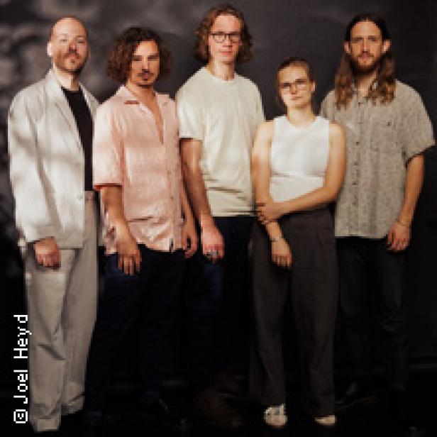 Fünf Bandmitglieder posieren vor einem dunklen Hintergrund.