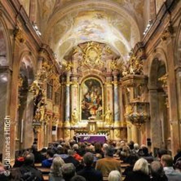 Innenansicht einer reich verzierten Kirche mit Menschen, die einer Zeremonie beiwohnen.