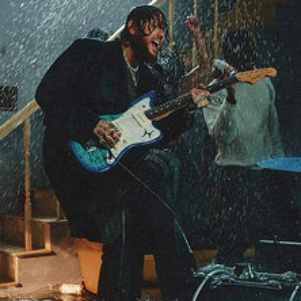 Ein Mann mit Tätowierungen spielt Gitarre, während es regnet.