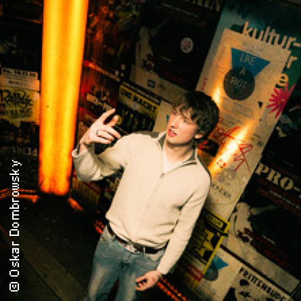 Ein junger Mann steht vor einer Wand voller Konzertplakate.