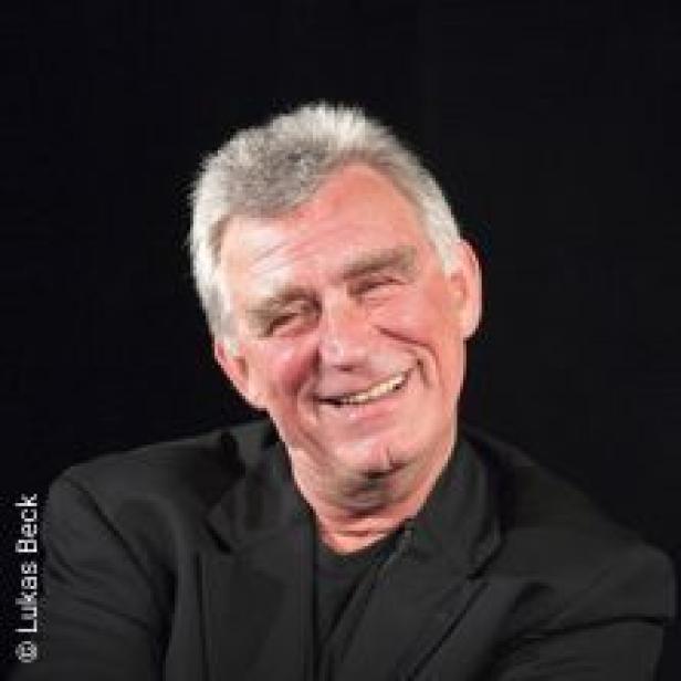 Ein älterer Mann mit grauem Haar lächelt in die Kamera.