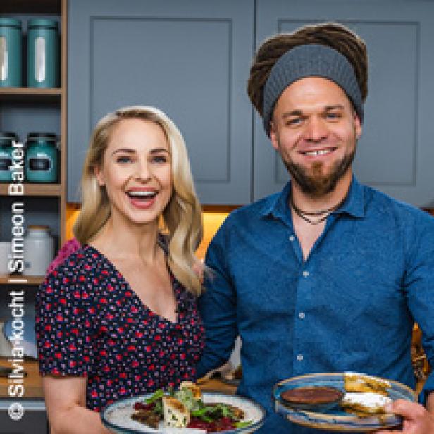 Eine lächelnde Frau und ein lächelnder Mann präsentieren Teller mit Speisen.