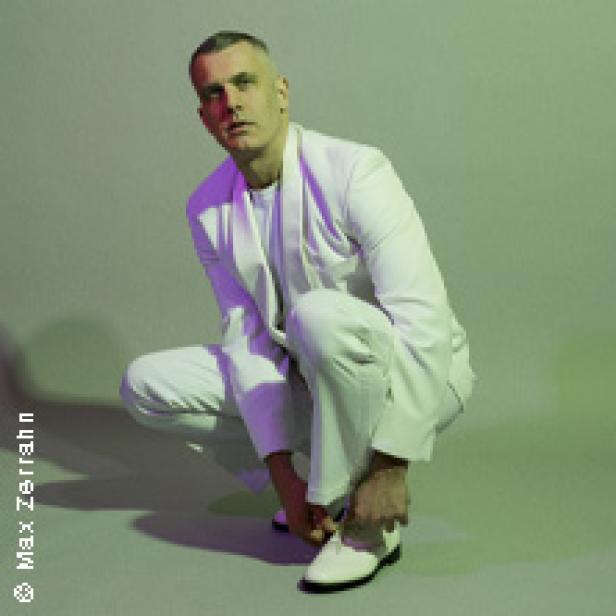 Ein Mann in einem weißen Anzug kniet und bindet seine weißen Schuhe.