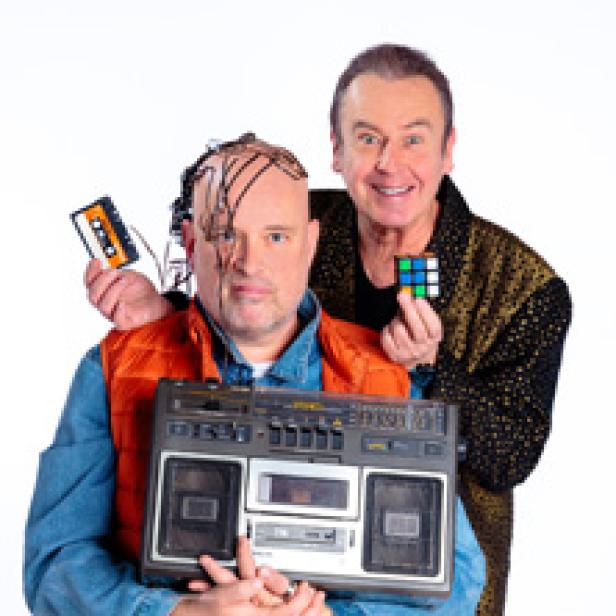 Zwei Männer posieren mit einem Ghettoblaster, einer Kassette und einem Zauberwürfel vor einem weißen Hintergrund.