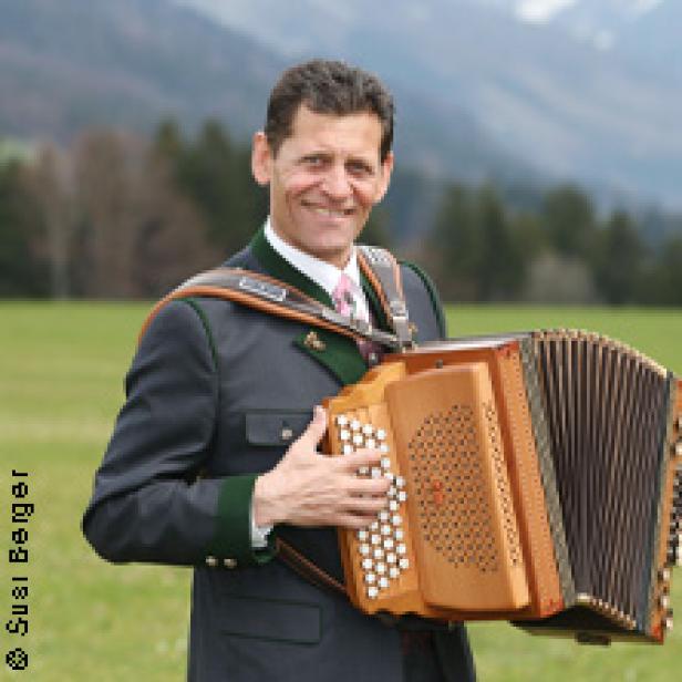 Ein Mann in Tracht hält eine steirische Harmonika in der Hand.