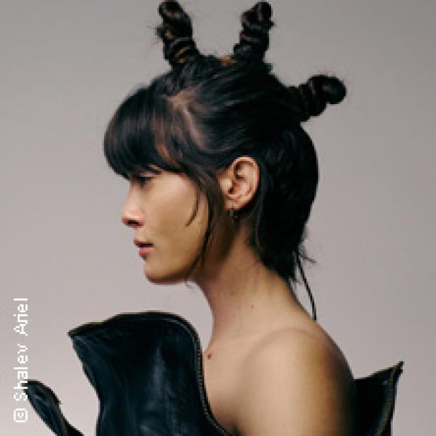 Eine Frau mit Pony und hochgesteckten Haaren, von der Seite fotografiert.