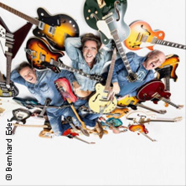 Drei Männer liegen auf dem Rücken, umgeben von vielen Gitarren.