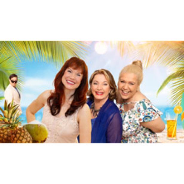 Drei Frauen lächeln vor einem tropischen Hintergrund in die Kamera.