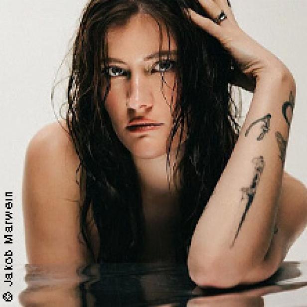 Eine Frau mit Tätowierungen posiert im Wasser.