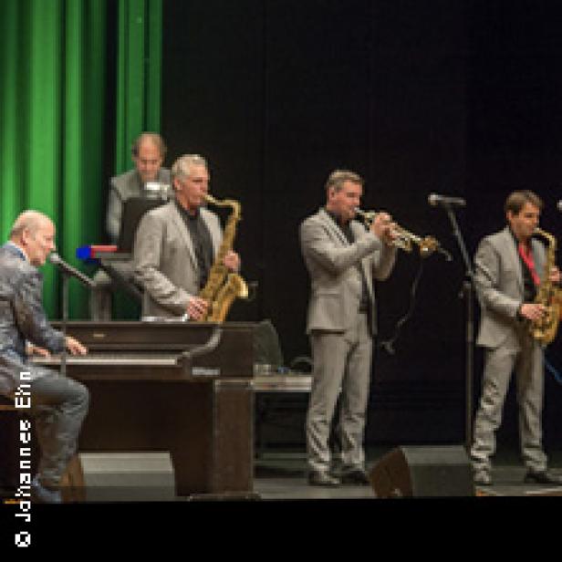 Eine Jazzband spielt auf einer Bühne mit grünen Vorhängen.