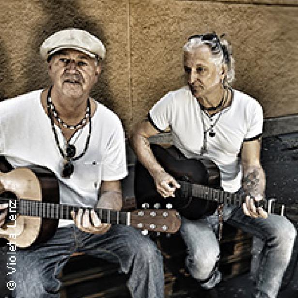 Zwei Männer sitzen draußen und spielen Gitarre.