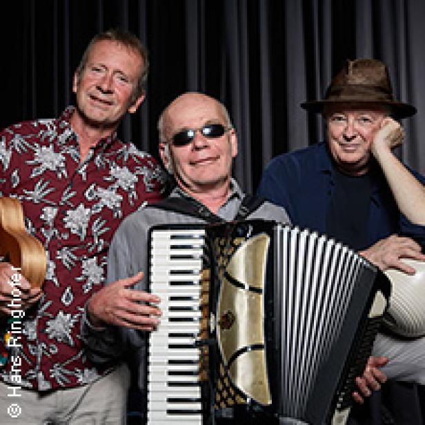 Drei Musiker posieren mit Akkordeon, Ukulele und einem weiteren Instrument vor einem dunklen Hintergrund.