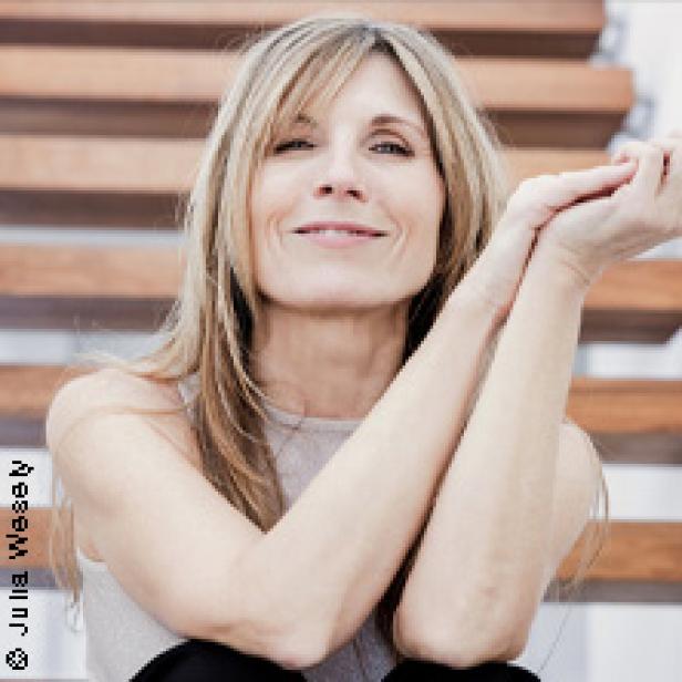 Eine Frau mit blonden Haaren sitzt lächelnd auf einer Holztreppe.