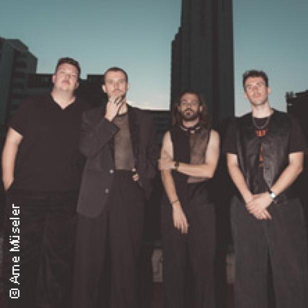 Vier Männer posieren vor einem hohen Gebäude für ein Foto.